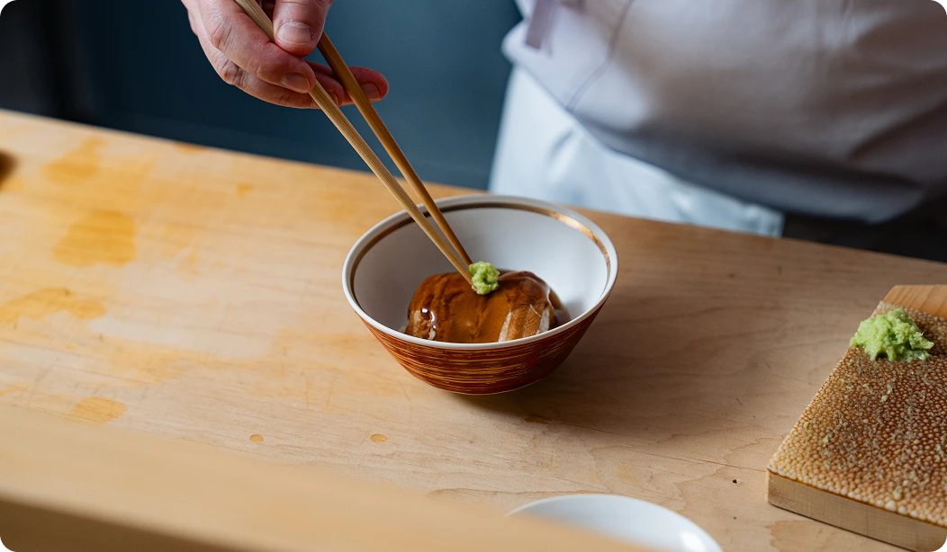茶碗に入った料理に、箸でわさびを添えている様子