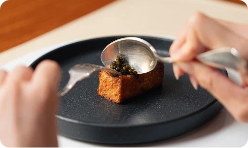 黒いお皿に乗った料理に、スプーンでキャビアのような具材を盛り付けている様子